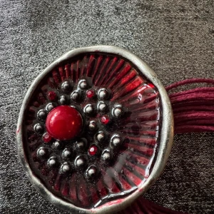 Rött och silverfärgat halsband med rund hängare - Unikt halsband med flera röda trådar och ett stort runt hängare i rött och silver. Hänget har en upphöjd röd mittpunkt och små silverfärgade kulor i ett mönster. Justerbart med kedja och lås i silverfärg. Perfekt för dig som gillar statement-smycken.