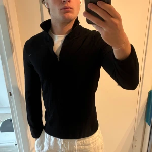 Svart merinoullströja från Riley half zip - Svart långärmad tröja från Riley i mjuk merinoull. Tröjan har en stilren half zip-dragkedja vid kragen och en klassisk passform. Perfekt för lager-på-lager och funkar året runt när du vill ha en clean look. Bra skick, passar även S