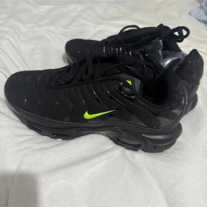 Nike Air Max Plus svarta med neon - Nike Air Max Plus sneakers i svart med neongröna detaljer och synlig air-sula. Ovandel i mesh och syntet med vågformade paneler, klassisk snörning och tydlig TN-logga under sulan. Snygg kontrast mellan svart och neon, perfekt för dig som gillar streetstyle.