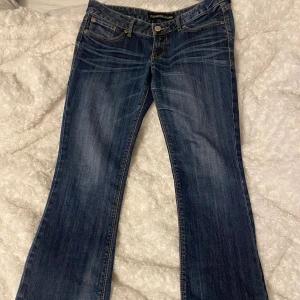 Blå lågmidjade bootcut jeans  - Snygga blå lågmidjade jeans från Express med bootcut-modell. Jeansen har en mörk tvätt med slitningar och kontrastsömmar samt broderade bakfickor. Köpt på plick, själv aldrig använt. Midjemått: 42cm. Innerbenslängd: 75cm 