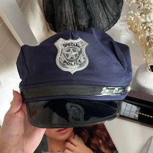 Poliskeps med silvermärke - Mörkblå poliskeps med blank svart skärm och ett stort silverfärgat polisemblem framtill. Perfekt till halloween. Aldrig använd. Föreslå gärna pris