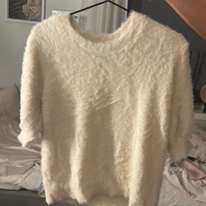 Fluffig beige tröja från Vero Moda - Supermjuk och fluffig beige tröja från Vero Moda. Tröjan har rund halsringning och halv-långa ärmar. Perfekt för dig som vill ha en mysig och trendig look med lite extra textur. Passar till både jeans och kjol för en chill vibe.