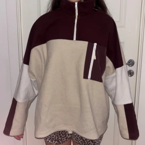 Beige och vinröd fleece från Monki - Säljer en oversized fleece från Monki i beige och vinrött med vit dragkedja och bröstficka. Tröjan har hög krage, half zip. 