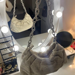 Beige axelväska med kedja - Jätte fin beige axelväska i tyg, får plats mycket i väskan. Köpte i en butik i London. 