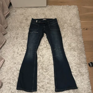 Bootcut jeans från Gina Tricot, mörkblå - Mörkblå bootcut jeans från Gina Tricot med snygga slitningar och kontrastsömmar. Klassisk femficksmodell med låg midja och utsvängda ben. Jeansen är gjorda i stretchigt denim för en bekväm passform.