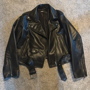 Svart skinnjacka från Zara med bälte - Säljer min svart skinnjacka från Zara med silvriga dragkedjor, fickor och bälte i midjan. Jackan är i storlek XL men liten i storleken så funkar till S och M. Jackan är använd bara några få gånger så den är i ett mycket bra skick.💕