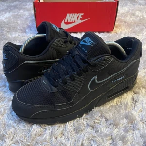 Nike Air Max 90 helsvarta sneakers - Snygga Nike Air Max 90 sneakers i helsvart med diskreta grå detaljer och klassisk siluett. Ovandel i mesh och syntet, ikonisk Air Max-dämpning i sulan och tydlig Nike-logga på sidan. Perfekta för dig som gillar stilrena och sportiga skor. Lite slitna vid hälarna men märks inte vid användning. Storlek 45
