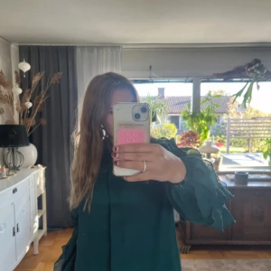 Mörkgrön volangblus med långa ärmar - Säljer en mörkgrön blus med långa ärmar och volangdetaljer. Blusen har en lös passform och är perfekt för dig som gillar en stilren men ändå lekfull look. Materialet känns lätt och flowy, och färgen är riktigt snygg till både sneakers och boots.