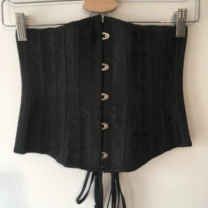 Svart Korsett - Bärs under brösten med en annan topp undertill. Hakar fram och snörning bak. Köpt secondhand. Säljer en liknande i vit!