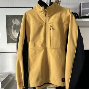 Klargul damjacka från Haglöfs 42 - Softshell jacka i klargult från Haglöfs.  Några fläckar på en ärm, se bild. I övrigt fint skick. 🌻  Storlek 42.   