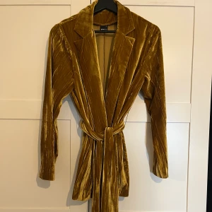 Velourkavaj Gina tricot - Superhärlig, mjuk och framför allt cool kavaj i guldig velour, köpt på Gina Tricot. Knytskärp i midjan.