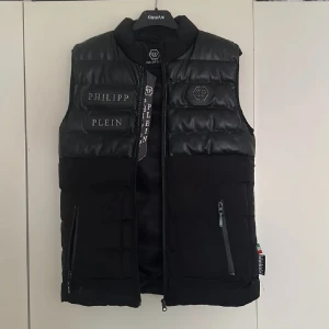 Väst - En svart Philip-plein väst i storlek S med fräcka ditaljer, 2 fickor med dragkedja 1 inne ficka. Ena drag kedjan går ej och öppna annars jätte bra skick, bästa kvalite inga skador!