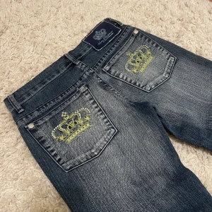Lågmidjade Victoria Beckham jeans - Säljer ett par lågmidjade Victoria Beckham jeans, helt nya. ❤️ Lågmidjad och bootcut/flare modell med kronor och rhinestones på backfickorna. Midjemått: 34,5cm och innerbenslängden 83cm. Köpare står för frakt! 