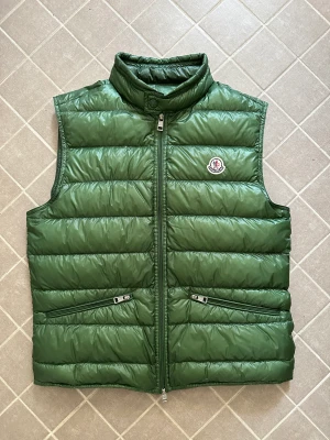 Moncler Gui - En Moncler Gui Väst i storlek 3 (L) men sitter lite mindre. Den är i bra skick förutom att det är ett litet hål på ryggen. Äkthets bevis finns. 