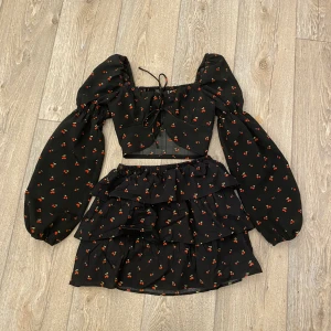 Somrigt Set - Både gulligt och smickrande set. En volangkjol och toppen har puffiga ärmar och en snygg knyt detalj över bröstet. Köpte sommaren 2022, använt cirka 3 gånger. Tyvärr är den för liten för mig. Den är inte för någon med stor byst! 