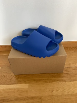 Yeezy Slide Azure - Helt nya Yeezy Slide Azure i storlek 43 (passar 41/42) säljes. Inköpta via Adidas CONFIRMED och digitalt kvitto finns.  Hämtas i Örnsköldsvik eller skickas på köparens bekostnad.