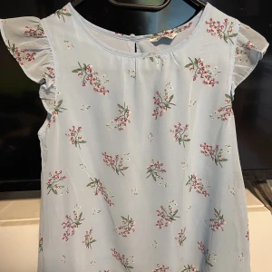 Blus  - Fin ljus blå blommig blus med volang på axeln! Dubbelt tyg! Aldrig använd ! Storlek 158