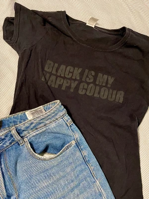 Basic svart T-Shirt EMP - Perfekt basplagg för alla årstider, sitter ganska tight och är styv i tyget så det blir inte mycket linjer från BHn. Text ”Black is my happy color”. Köpt på EMP, märket är Fruit of the loom. 