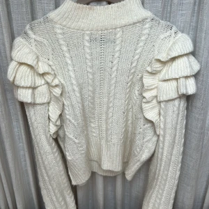 Volang tröja  - Säljer denna super fina stickade tröjan med volang axlar, den har en liten fläck vid halsen, annars super bra skick📦💓