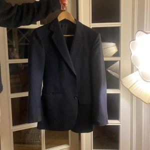 Marinblå kavaj - Här är en vintage kavaj i tjockare material med snygga spetsiga axlar och en indragen midja. Kavajen är marinblå med tunna ränder i färgerna blå och röd❤️