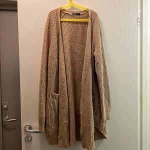 Kofta  - En knälång beige kofta från Gina. Väl använd. Och kan behövas lagas med två enkla stygn. Storlek XL.  I den kan man mysa med en stor kopp te, i ett fönster och romantisera sin vardag🥰😙