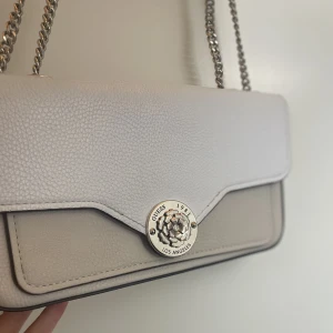 GUESS väska - Super fin GUESS väska, som jag tyvärr inte får användning av. Den är i färgerna vitt, beige och guld.  Den är använd men knappt några slitage alls. Du kan hänga väskan både över kroppen och över axeln. Org pris ca 2000kr Köparen står för frakt, tar Swish😊