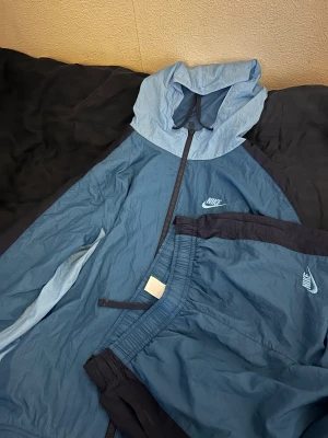 Nike Blå Tracksuit - En jättefin Nike tracksuit i storlek S, jätte fin förg ser lite annorlunda ut pga ljuset. Kan tänka mig att gå ner i pris.