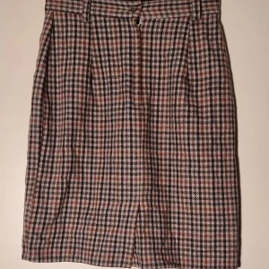 Kjol - Elegant lite tjockare kort kjol med innefoder. 65% ull.  Dragkedja och knäppning bak. Inga fickor.  