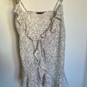 Överlappande klänning - Blommig klänning. Aldrig använd. Snörning med överlappande. Går strax över mitten på låret på mig som är 165 cm.