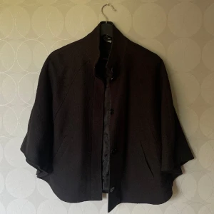 Kappa - Svart kappa/poncho då den inte har några ärmar. Minns tyvärr inte vart jag köpte den. Faller väldigt fint, är i fint skick. Stängning med gömda knappar, ser väldigt elegant ut.