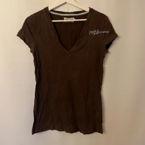 T-shirt Peak - Brun v-ringad tshirt med blå text. Märke: Peak performance. Storlek: S