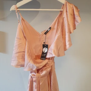 Rosa satin omlottklänning - Superfin wrap aroundklänning från boohoo. Man sveper den liksom omkring sig och knyter så midjan går att anpassa efter behov. Speciell design men en volangärm o ett vanligt axelband. Oanvänd med lapp kvar 🤗💕 fler bilder finns!