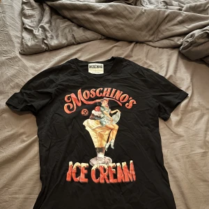 Moschinos ice cream T-shirt  - Moschinos ice cream T-shirt i storlek 48 vilket motsvarar M-L. Har ej kvitto på den men den är köpt på johnells. Skick 7/10, lite sliten i trycket men annars är den felfri. Pris går att diskuteras 