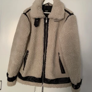 Teddyjacka - Beige teddyjacka med svarta fejkläder detaljer. Jackan är endast använd en gång! 