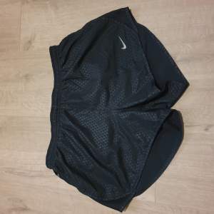 Korta dry-fit träningsshorts i märket Nike. Dragkedja till ficka bak på shortsen och innerbyxor. Storlek S