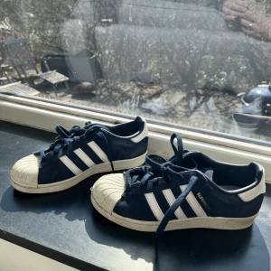Adidas superstar sneakers  - Ett par adidas superstar sneakers. Vita ränder och mörkblå mocka. Supersköna att gå i! Knappt använda. 