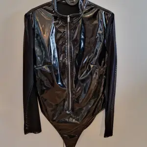 Latexliknande bodysuit med mesh-ärmar och dragkedja. Bra skick.