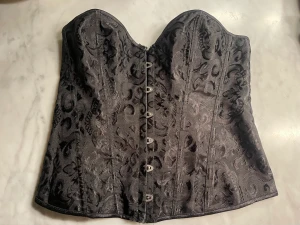Korsett (L men justerbar mindre/större) - Jättefin korsett nu till halloween eller bara allmänt. Storlek L. Kan dock justeras mindre/större beroende på hur hårt man snörar. Dock inget band där bak, men kan ta vilket snöre som helst skulle jag tro. 