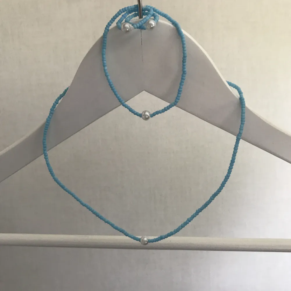Matchande set av ett halsband, två ringar ( en mellan och en stor ) och ett armband. Gjort av elastisk tråd och små blå och vita pärlor. Nya, oanvända och handgjorda. Halsband är 13 cm i diameter och armband 6 cm i diameter.  Köpare står för frakt.. Accessoarer.