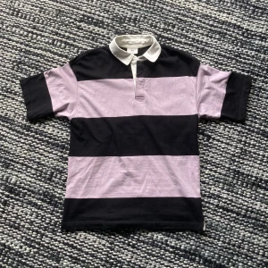 Rugbytröja - En svart/lila randig kortärmad tröja med vit krage. Oversized, står storlek S men sitter som M/L. Köpt i höstas och använd ungefär 5 ggr. Ascool 90tals britpop vibb på tröjan?! Tyvärr inte riktigt min stil längre :( Hör gärna av dig med frågor!!