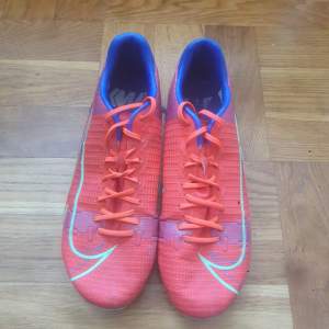 Ett par röda fotbollskor som har använts mycket men skorna håller fortfarande bra kvalitet. Skostorleken är 40,5