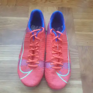 Ett par röda fotbollskor som har använts mycket men skorna håller fortfarande bra kvalitet. Skostorleken är 40,5