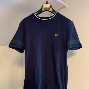 En mörkblå Lyle & Scott t-shirt i storlek S.  Mönster på både kragen och ärmarna där passformen är normal