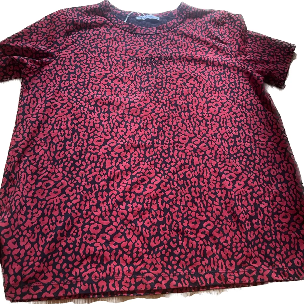 Röd och svart leopardmönstrad t-shirt med texten ”follow your intuition” (som förövrigt knappt syns?) . T-shirts.