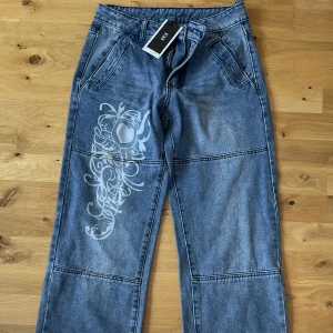 Jeans - Blå jeans från emmimol med ett tryck på knäet. Aldrig använda, prislapp kvar. Har en fläck, men vet ej varifrån. Däremot är fläcken knappt synlig. Medelhög midja
