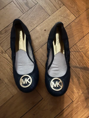 MK baklerina skor  - Nästan nya ballerina skor från MK (Michael Kors). Använt Max 3 gånger men insett att de är för små. Inget slitage på sulor eller utsidan av skorna och innersulan är hel och ren. Rengjorda och sprayade med skodeo. Storlek: 38 Färg: Marinblå Nypris: 899 kr 