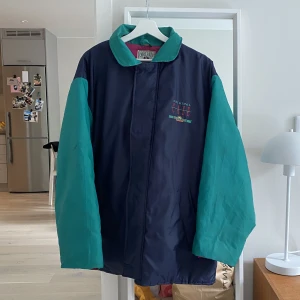 Vintage jacka - En mörkblå/grön/rosa oversized jacka med tryck både fram och bak. Det är en tunnare täckjacka med både dragkedja och knappar. Jättefin modell/passform men den är väldigt oversized, så skulle rekommenderas för någon lite längre person. 