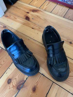 Black faux leather loafers with a small platform and fringe  