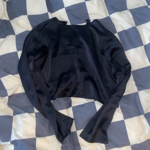 Satin crop top - Svart crop top i typ fejkad satin eller något! Glansig iallafall! Liten knapp i nacken så det blir en gullig liten öppning i ryggen! Från H&M. Aldrig använd, endast provad!