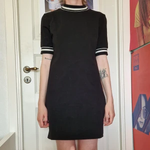 Svart tshirtklänning - Svart, tight tshirt-klänning med vita ränder runt ärmar och halsringning. Stretchig och superskön! Kan passa allt från XS–M beroende på hur du vill ha passformen.